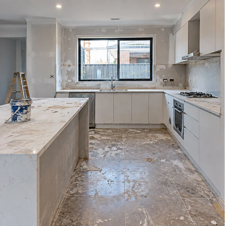 Kitchen renovation with dusty benchtops, plastered walls, a paint bucket and dirty tiled floors before a builders clean