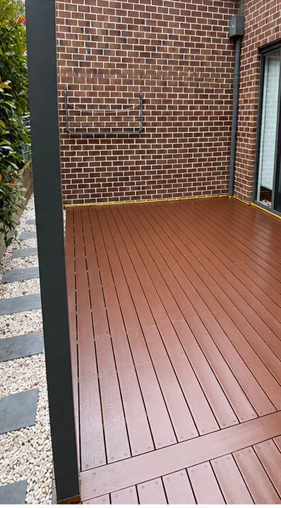 Timber deck freshly painted in a rich red-brown finish beside a brick wall