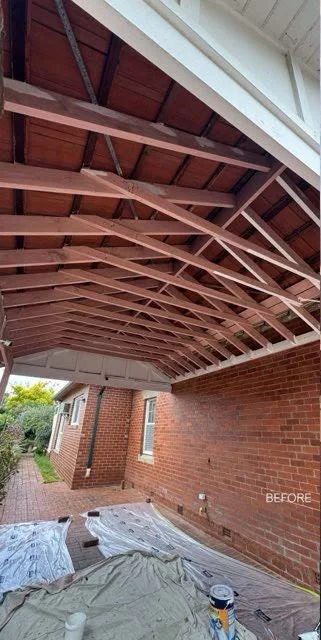 Weathered timber rafters under an outdoor roof with drop sheets laid below before painting