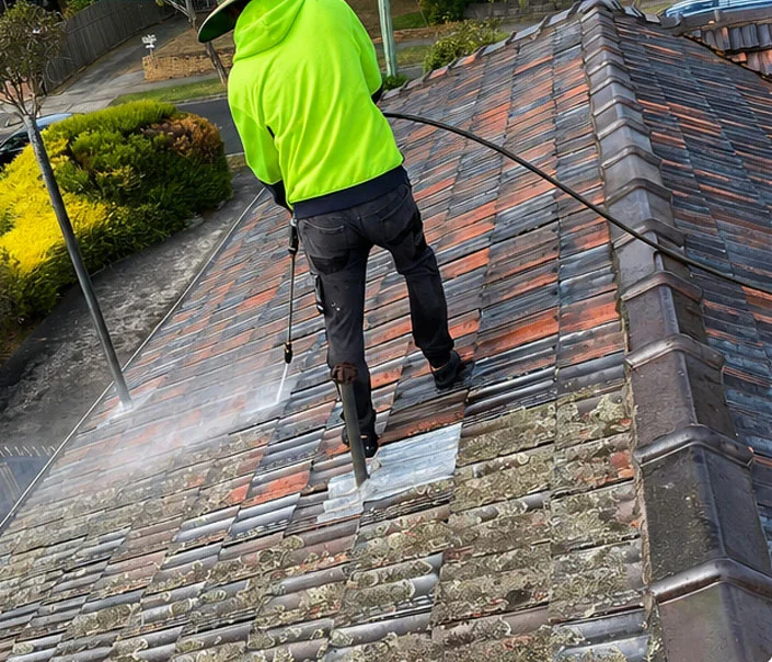 Technician in hi-vis pressure cleaning the roof, revealing clean terracotta tiles beneath the lichen