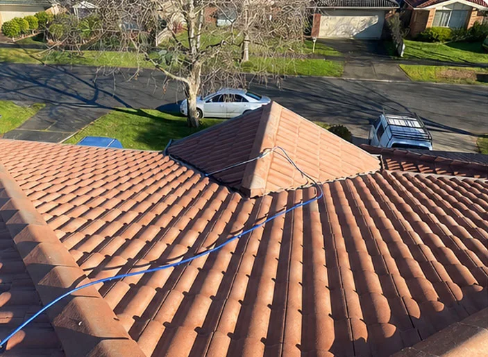 Faded, weathered terracotta roof tiles with a pressure cleaning hose laid across them before restoration